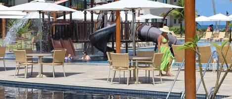 A pool area with a water slide, lounge chairs, and umbrellas.