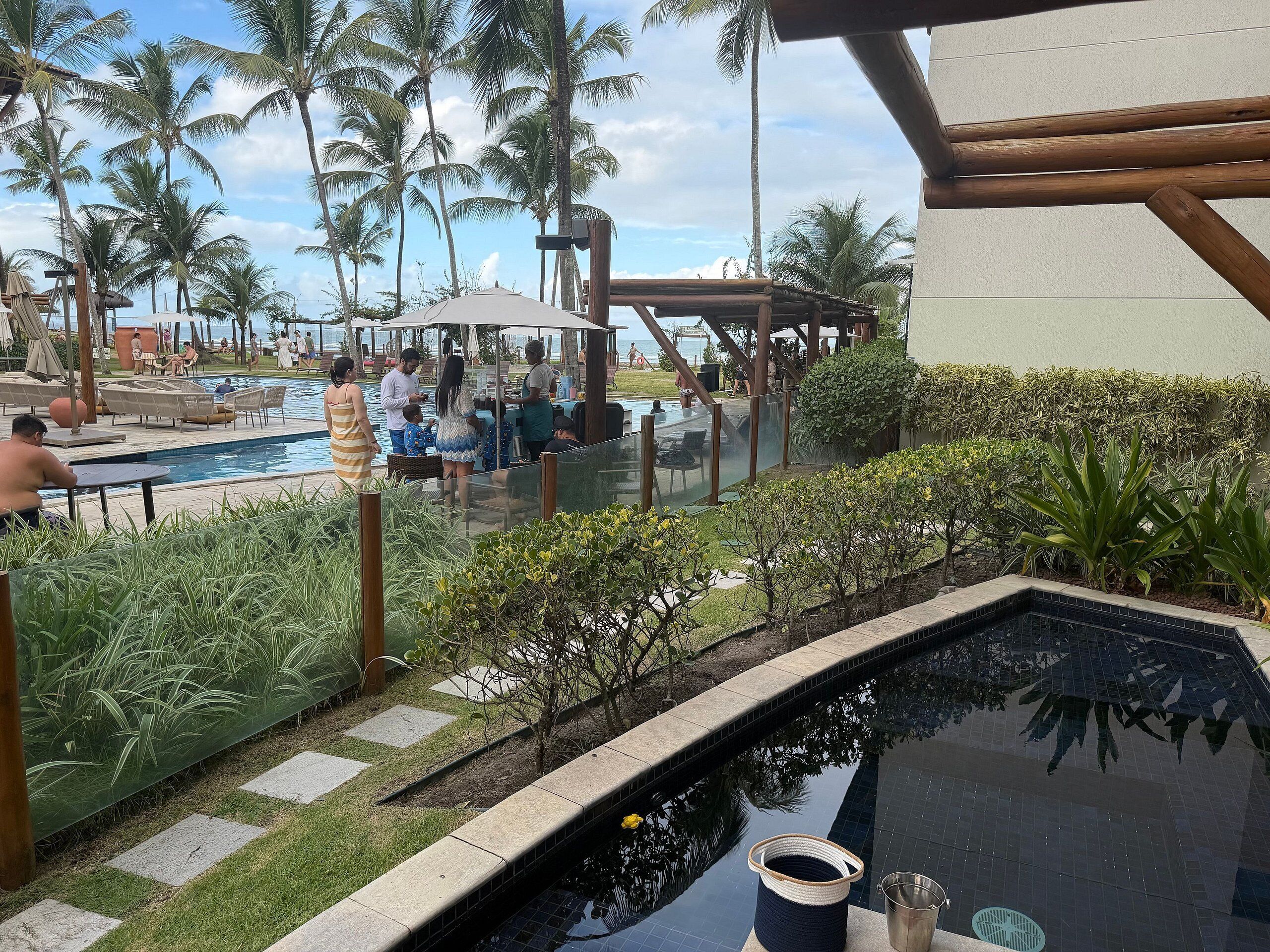 Uma área de piscina com espreguiçadeiras, uma piscina pequena e palmeiras.