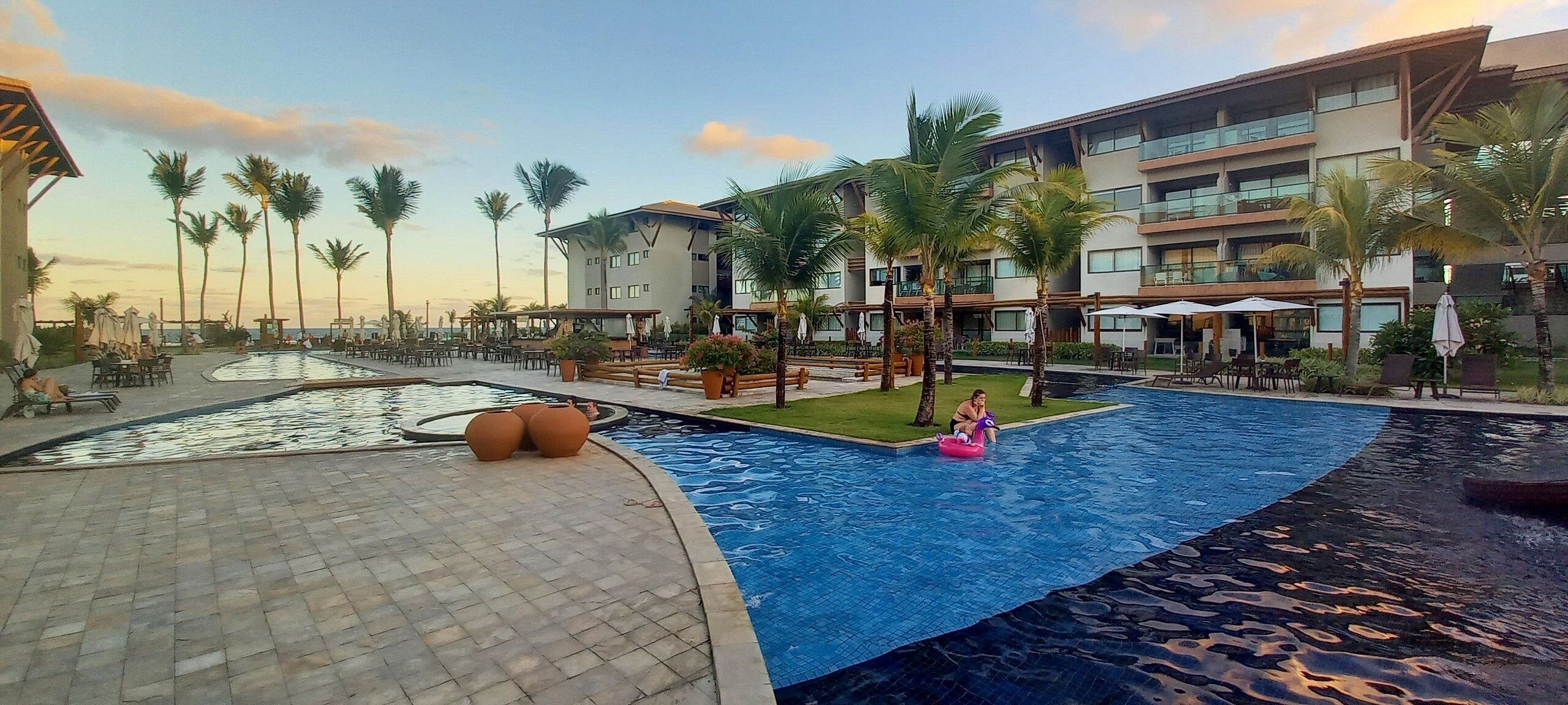 Ein Poolbereich eines Resorts mit großem Pool, Liegestühlen und Palmen.