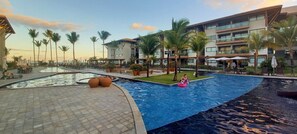 Zona de piscina en un resort, con una piscina grande, sillas de descanso y palmeras.