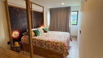 Un dormitorio con estructura de cama de madera, una mesita de noche, aire acondicionado instalado en la pared y una ventana con cortinas.