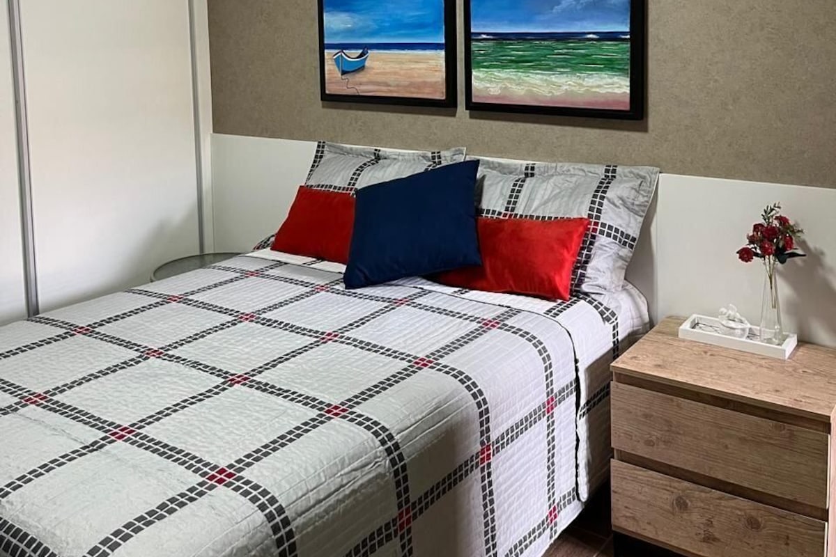 A bedroom with a bed, nightstand, and two framed pictures on the wall.