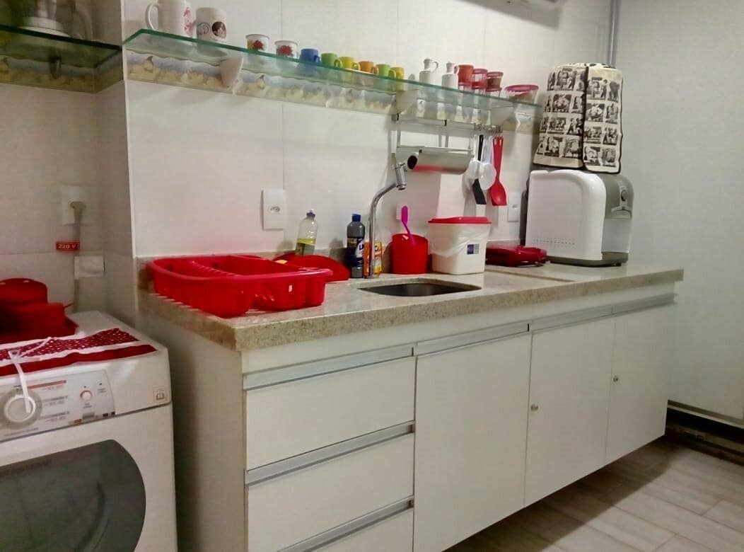 Una cocina con un lavamanos, lavadora y estante de vidrio con diversos utensilios de cocina.