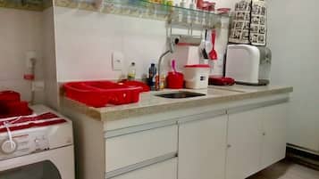 Una cocina con un lavamanos, lavadora y estante de vidrio con diversos utensilios de cocina.