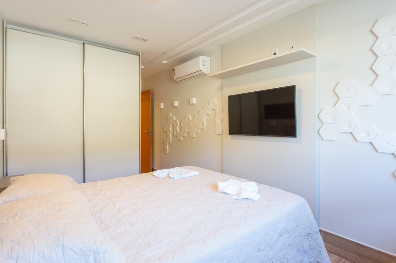 A hotel room with a bed, a TV, an air conditioning unit, and a wall with hexagonal patterns.