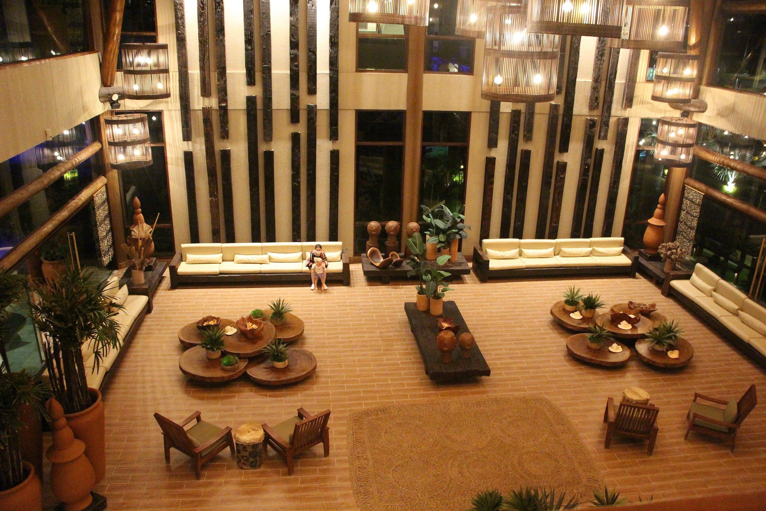 Um hall amplo com diversas áreas de estar, uma mesa de centro e plantas decorativas.