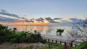 A coastal view with a sunset, calm sea, and a sandy beach with greenery in the foreground. -  Polinesia Resort - Porto de Galinhas - Acesso ao Hotel Samoa.  (Ipojuca)