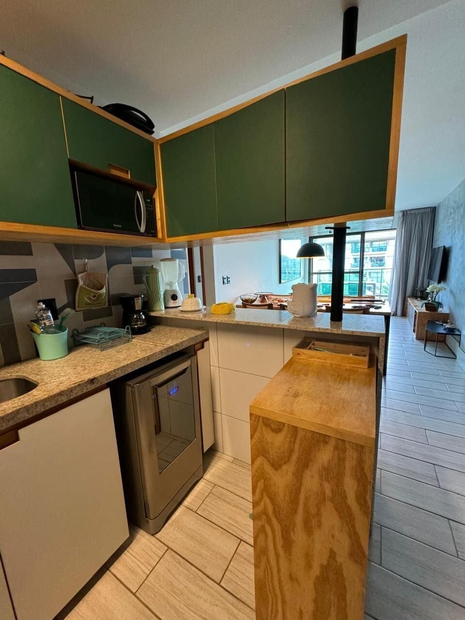 Cozinha moderna com armários verdes, micro-ondas embutido, máquina de café e lava-louças.