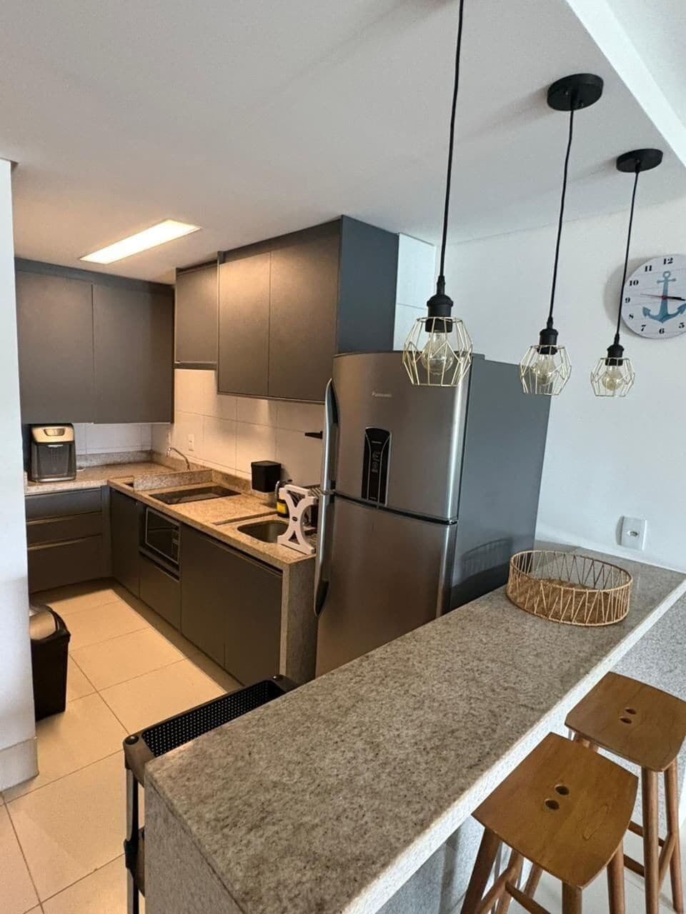 Eine moderne Küche mit Edelstahlkühlschrank, Granitarbeitsplatte und Pendelleuchten.