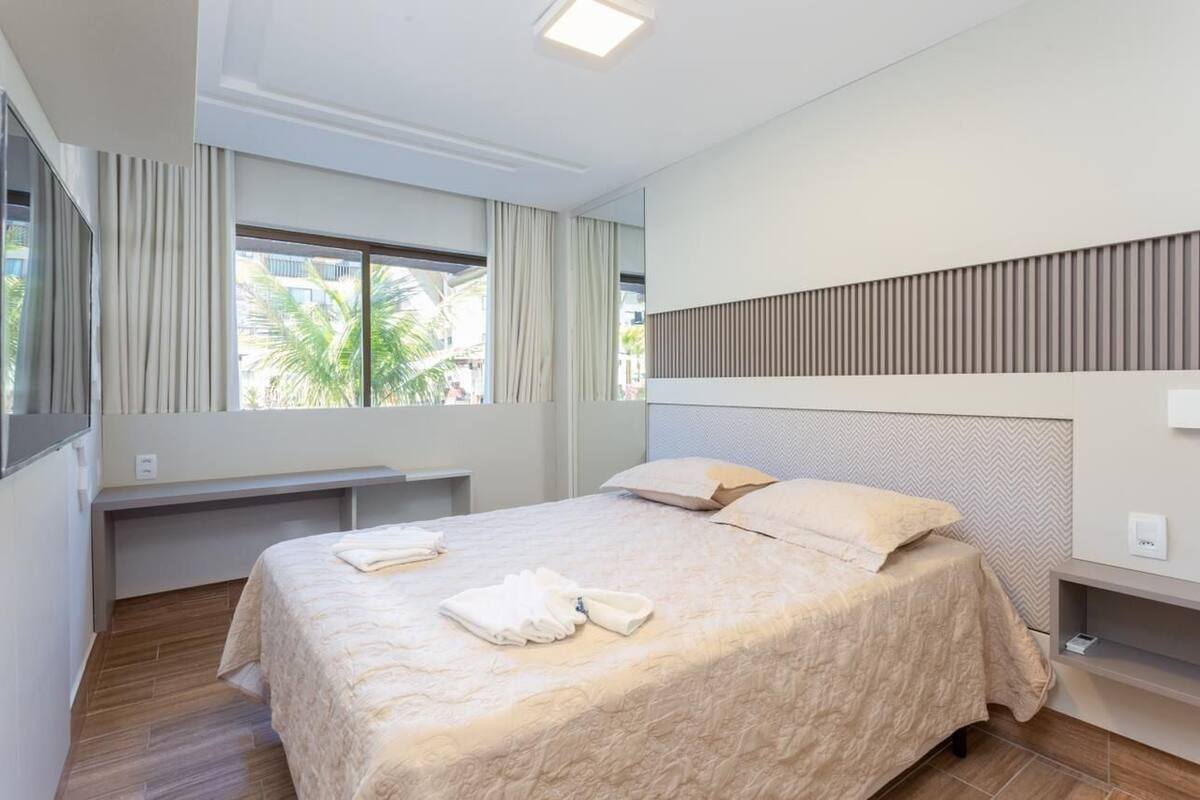 A hotel room with a bed, a window with curtains, a headboard, and a bedside table.