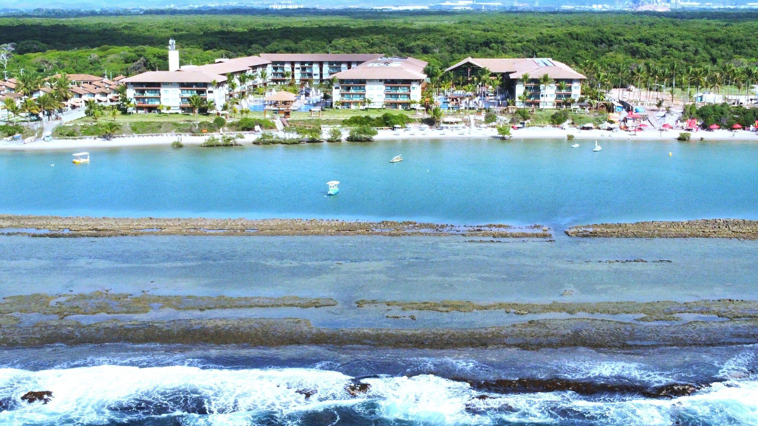 A coastal hotel with multiple buildings, a beach, and a rocky shoreline.