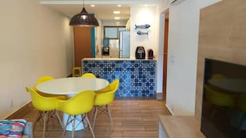 A dining area with a round table and yellow chairs, a kitchen with blue and white tiles, and a fish decoration on the wall.