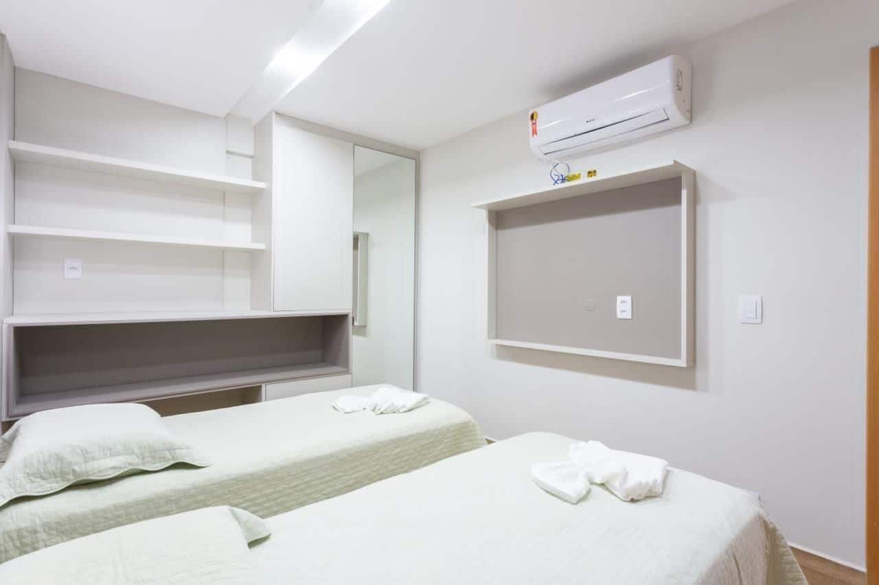 A hotel room with two beds, a large mirror, a wall-mounted air conditioner, and built-in shelving.
