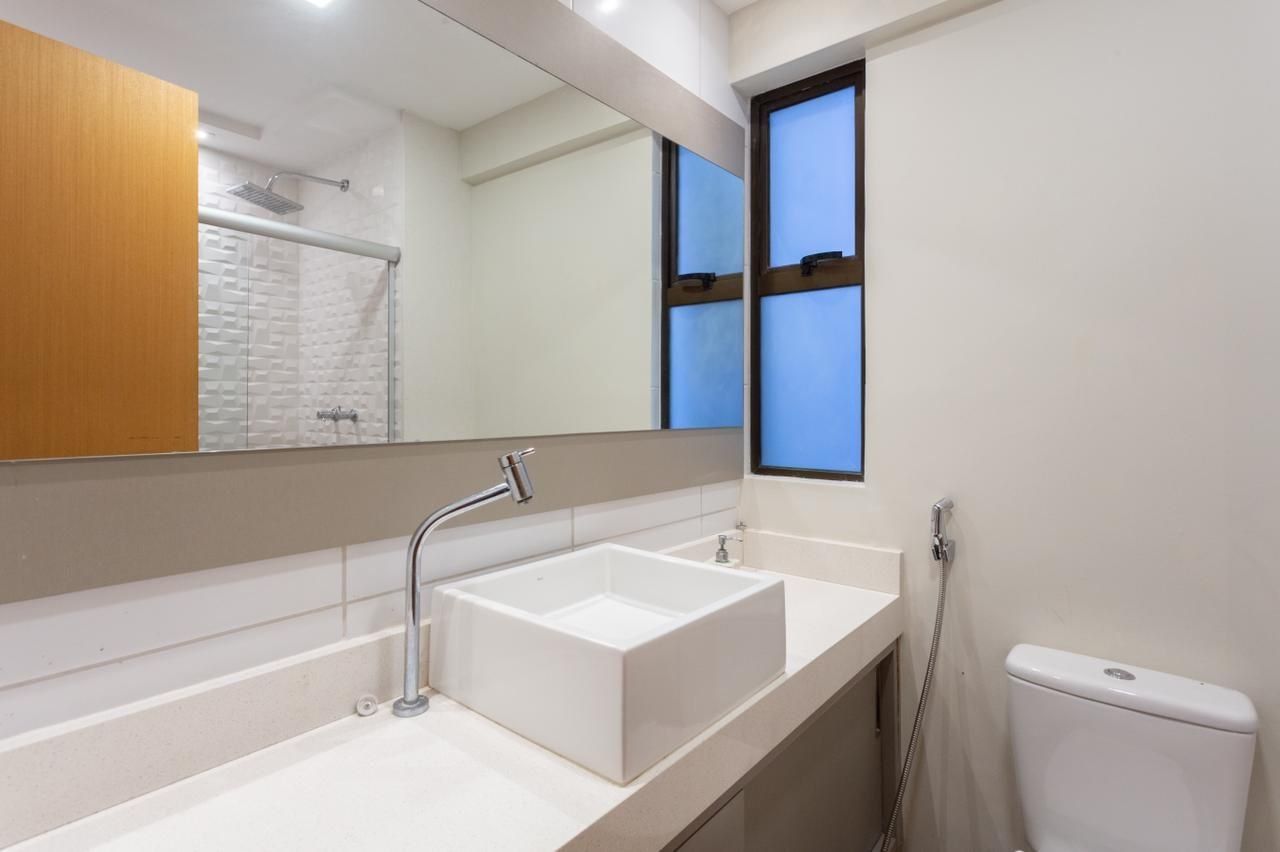 A modern bathroom with a large mirror, a white sink, a shower, and a toilet.