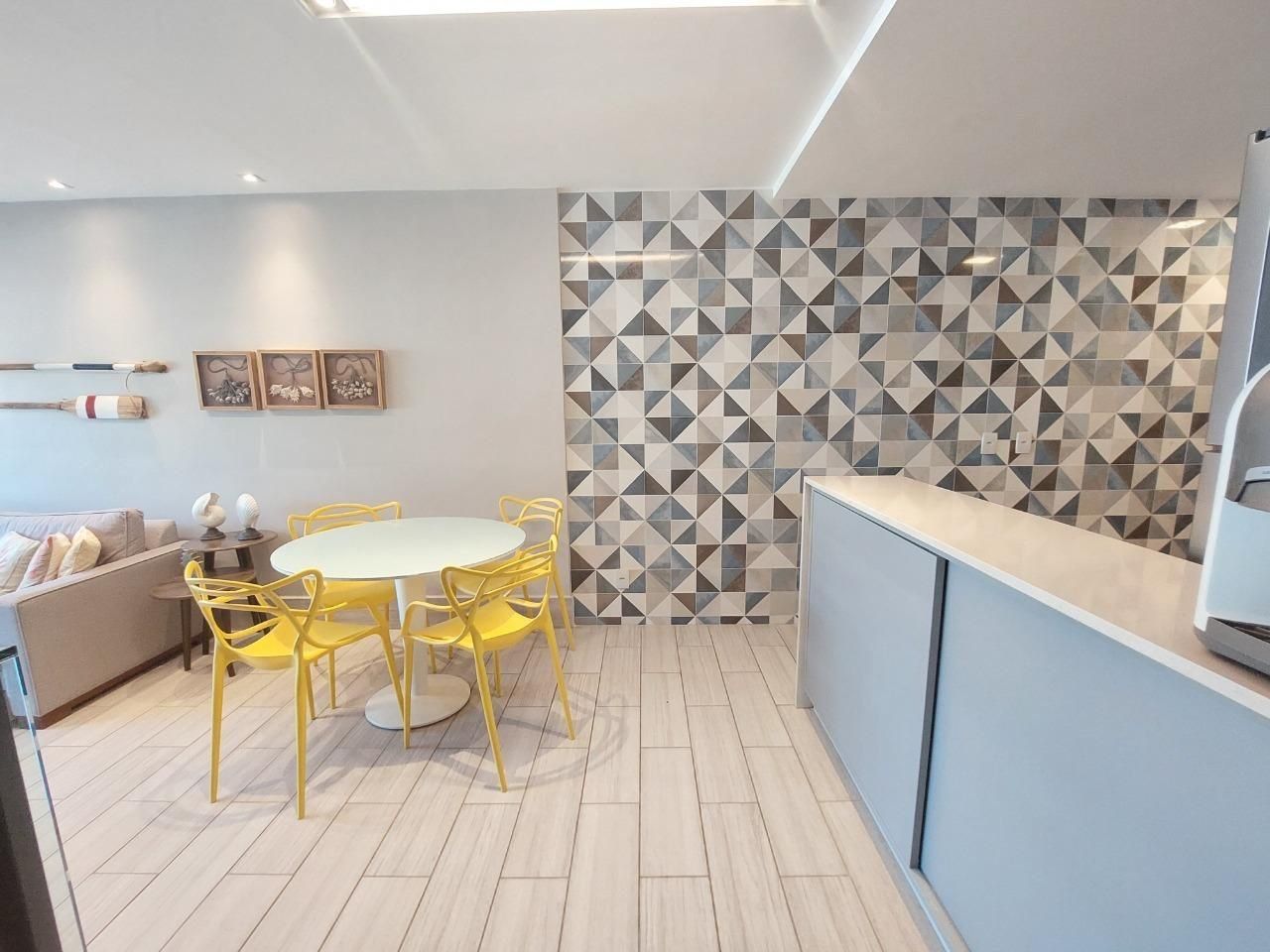 Une cuisine moderne avec un coin repas, agrémentée d’un dosseret de carrelage à motifs géométriques, d’une table à manger blanche avec des chaises jaunes et d’un plancher de couleur claire.