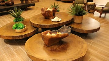 A lobby with round wooden tables, some with potted plants, and a central table with a decorative item.
