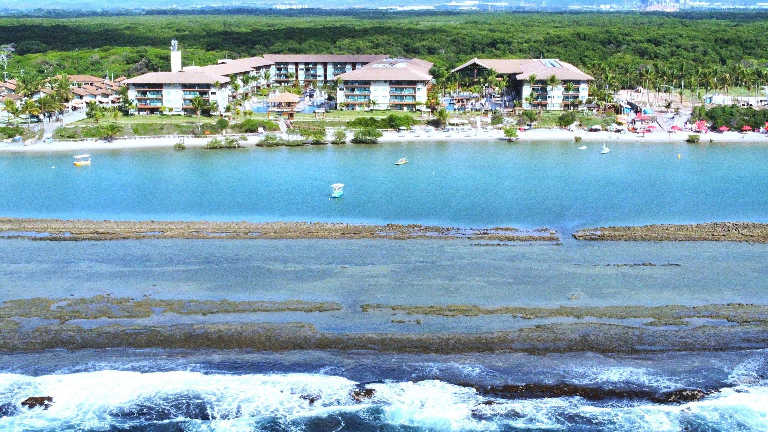 Un hotel frente al mar con varias construcciones, una playa y un litoral rocoso.