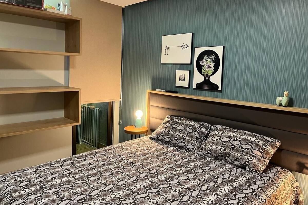 A bedroom with a bed, a nightstand, a wall-mounted shelf, and two framed pictures.