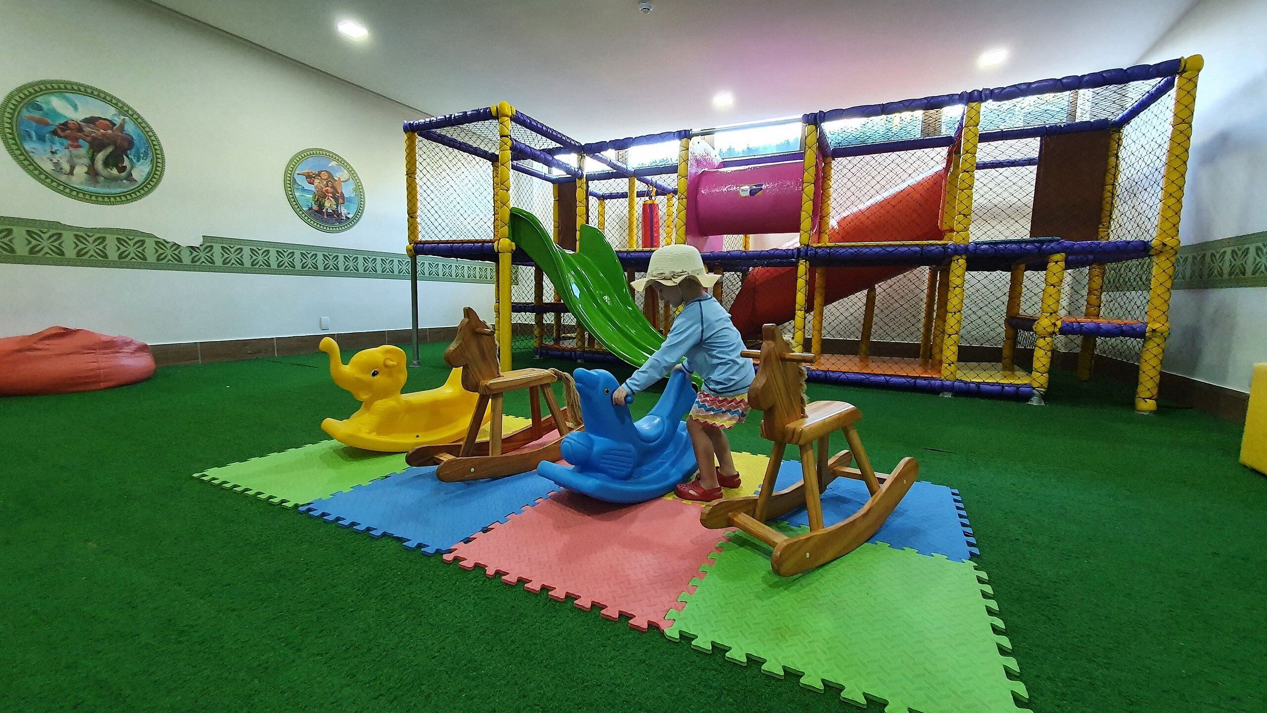 A play area with a climbing net, a slide, and colorful play mats.
