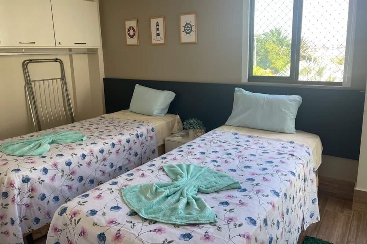 A room with two beds, a window with a view, a drying rack, and a wall with nautical-themed decorations.