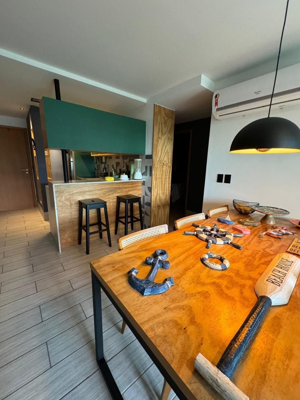 Una cocina moderna con una isla central, mesa de comedor de madera con decoración náutica y una lámpara colgante grande.