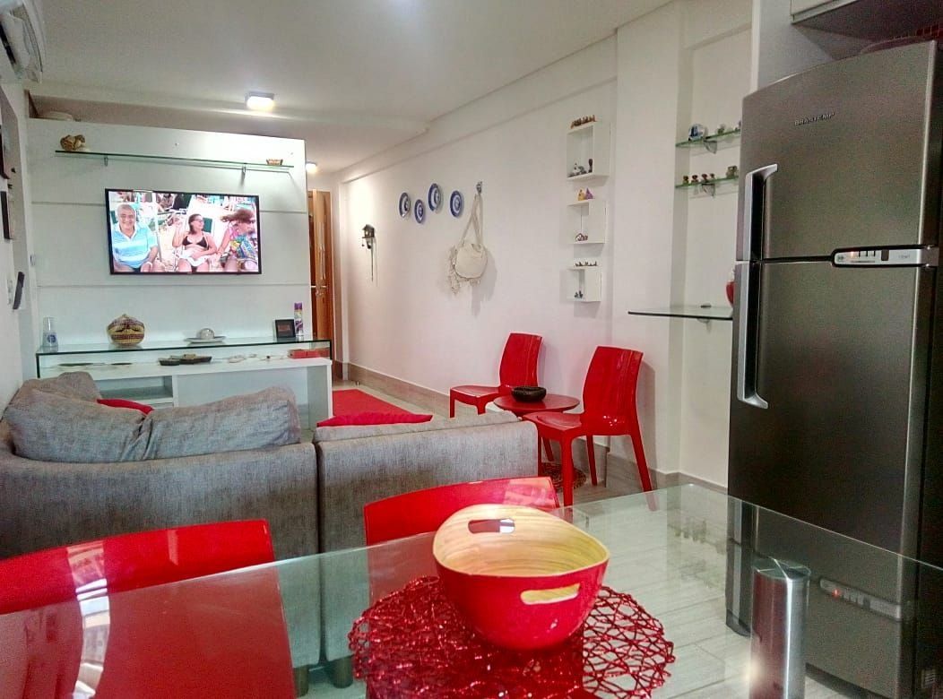 Una sala de estar moderna con una mesa de comedor de vidrio, sillas rojas, un sofá gris, un televisor de pantalla plana y un refrigerador de acero inoxidable.