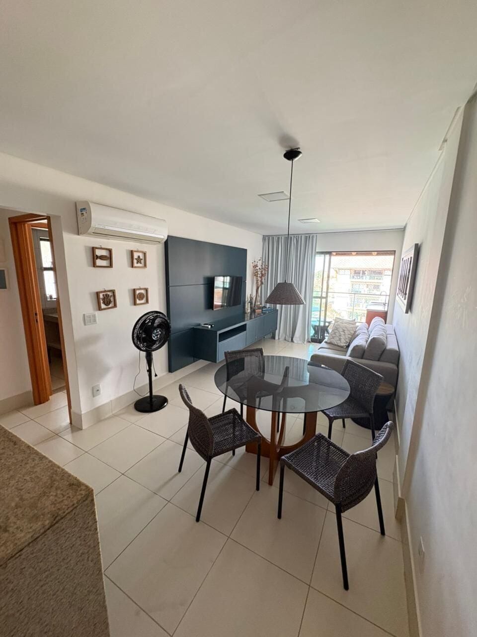A modern living room with a round glass table, dark sofas, and a TV mounted on the wall.