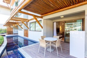 A modern outdoor pool area with a wooden pergola, a round table with chairs, and a glass door leading to an indoor space. -  Polinesia Resort - Porto de Galinhas - Acesso ao Hotel Samoa.  (Ipojuca)