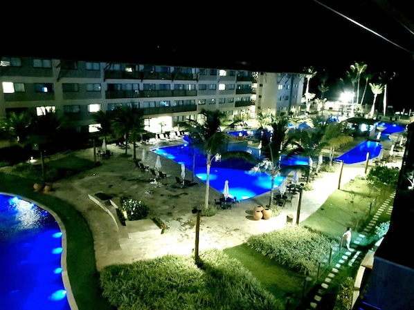 A hotel with multiple swimming pools, palm trees, and lounge chairs.