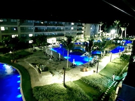 A hotel with multiple swimming pools, palm trees, and lounge chairs.