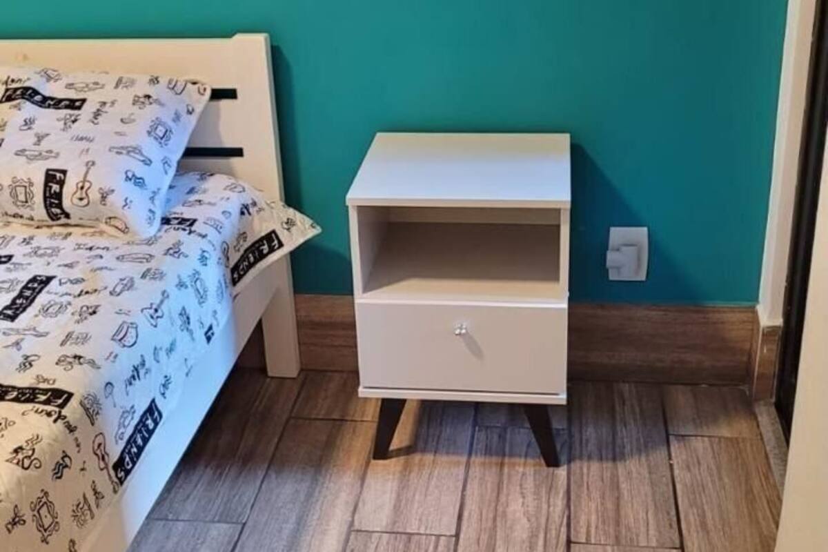 A room with a bed, a white nightstand, and a teal wall.