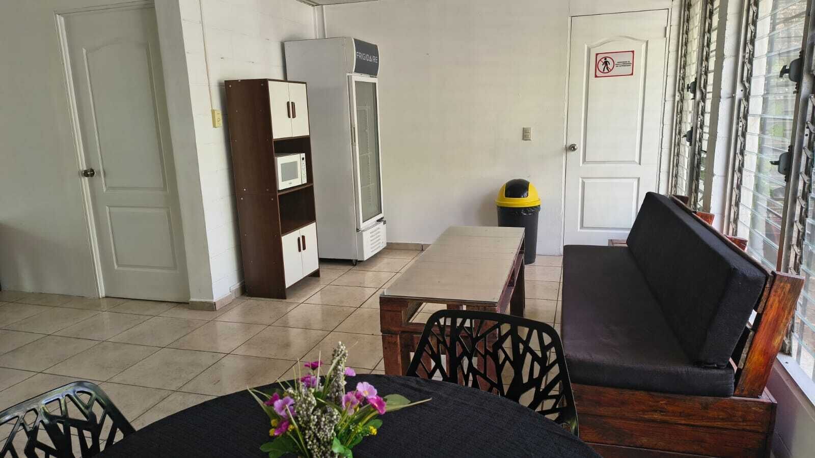 Een kamer met een bank, een tafel met een bloemenvaas, een magnetron en een koelkast.