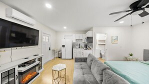 A modern living room with a fireplace, grey sofa, flat-screen TV, and a ceiling fan.