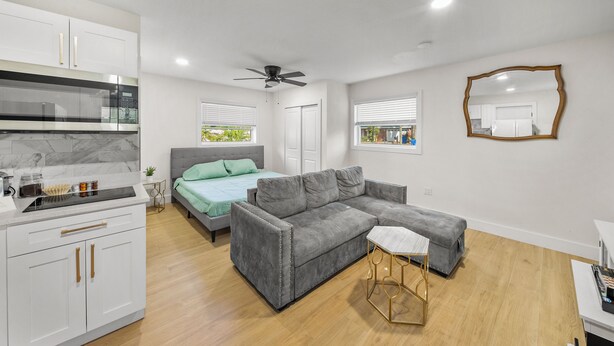 A modern bedroom with a grey sectional sofa, a small white table, and a ceiling fan.