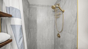 A walk-in shower with a gold showerhead and a handheld shower attachment.