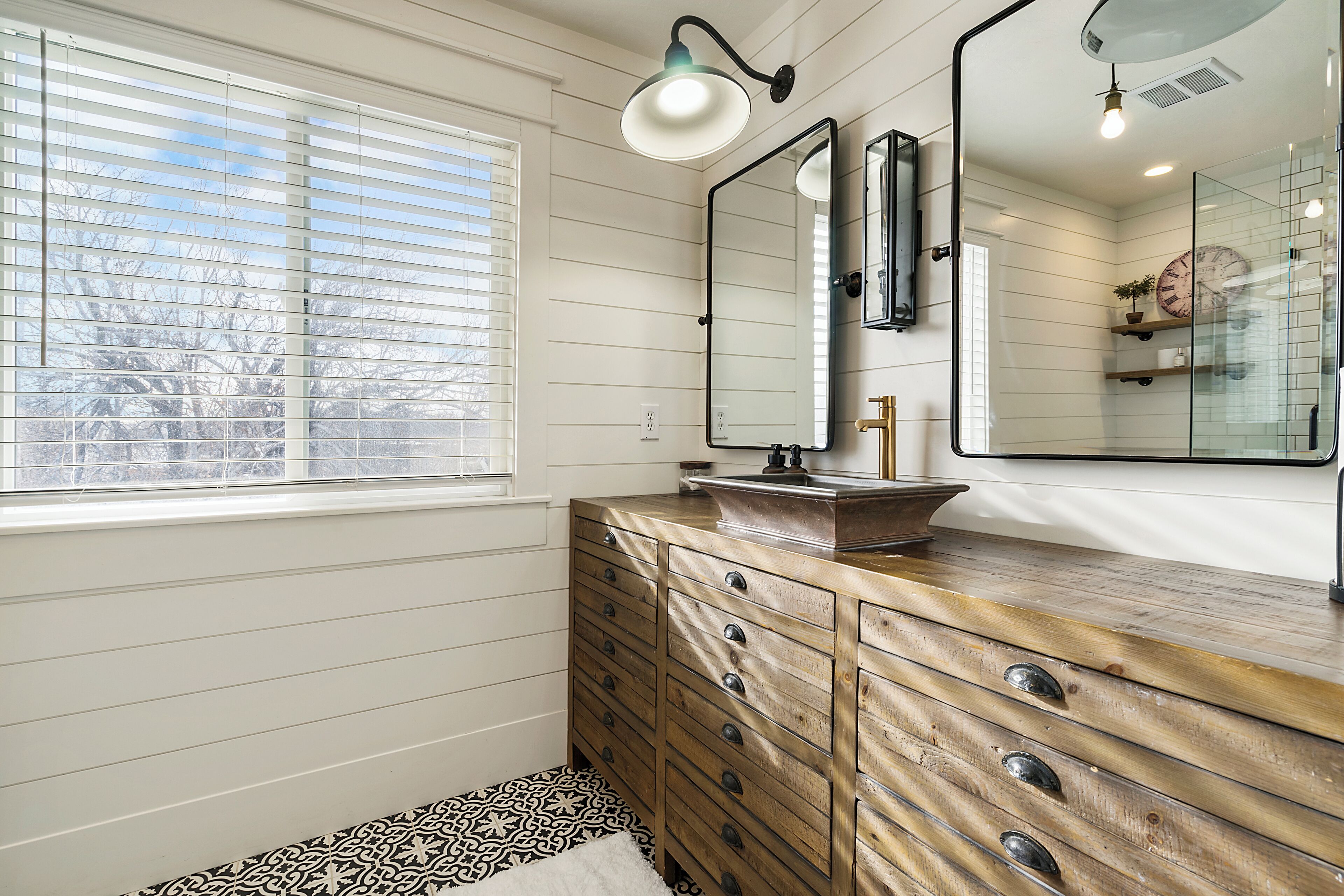 A bathroom with a wooden vanity, a large mirror, and a window with blinds.
