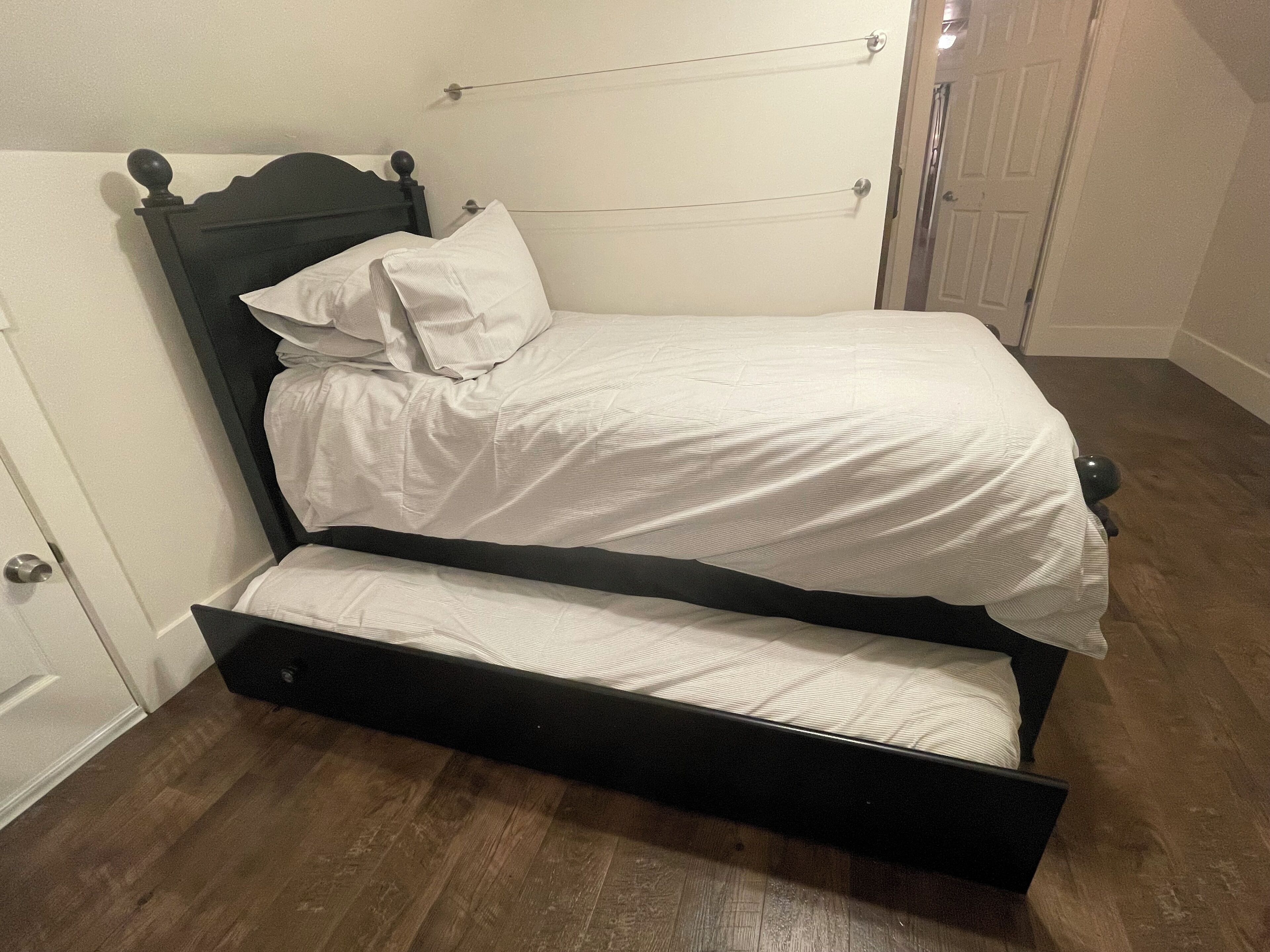 A single bed with a wooden frame and a black headboard, accompanied by a white mattress and pillows.
