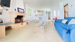 A modern living room with a fireplace, a blue sofa, and a dining area with white chairs. - A step away from the beach, first line, incredible views brand new! (Puerto de Mazarrón)