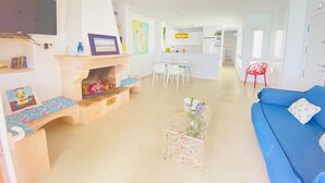 A modern living room with a blue sofa, a fireplace, a dining area, and a kitchen in the background. - A step away from the beach, first line, incredible views brand new! (Puerto de Mazarrón)