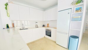 A modern kitchen with white cabinets, a built-in oven, a sink, and a blue trash bin. - A step away from the beach, first line, incredible views brand new! (Puerto de Mazarrón)