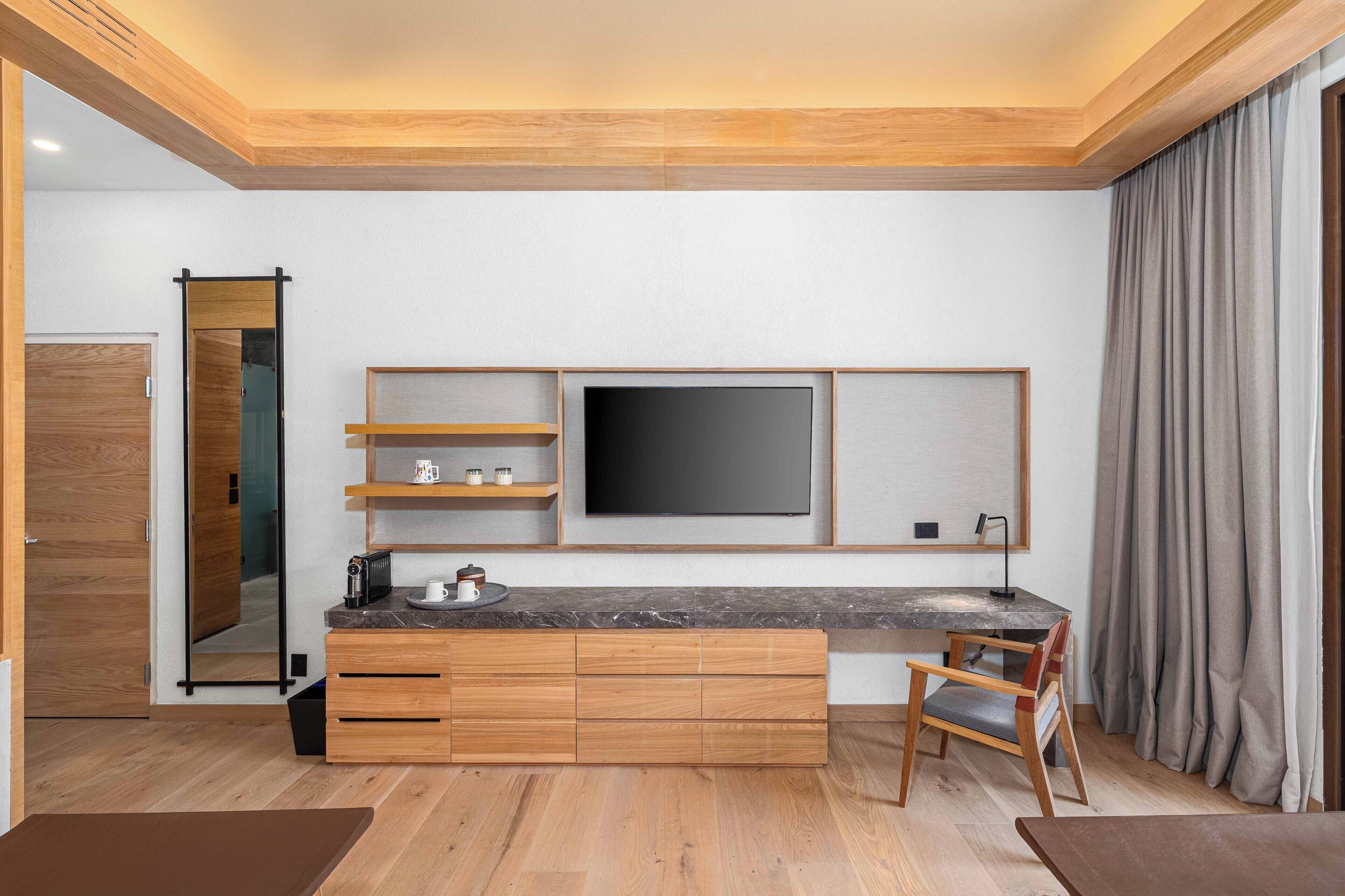 A modern kitchen with wooden cabinetry, a built-in TV, and a dining area with a chair.