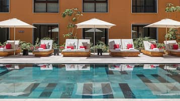 Una piscina al aire libre, sombrillas, sillones reclinables de piscina