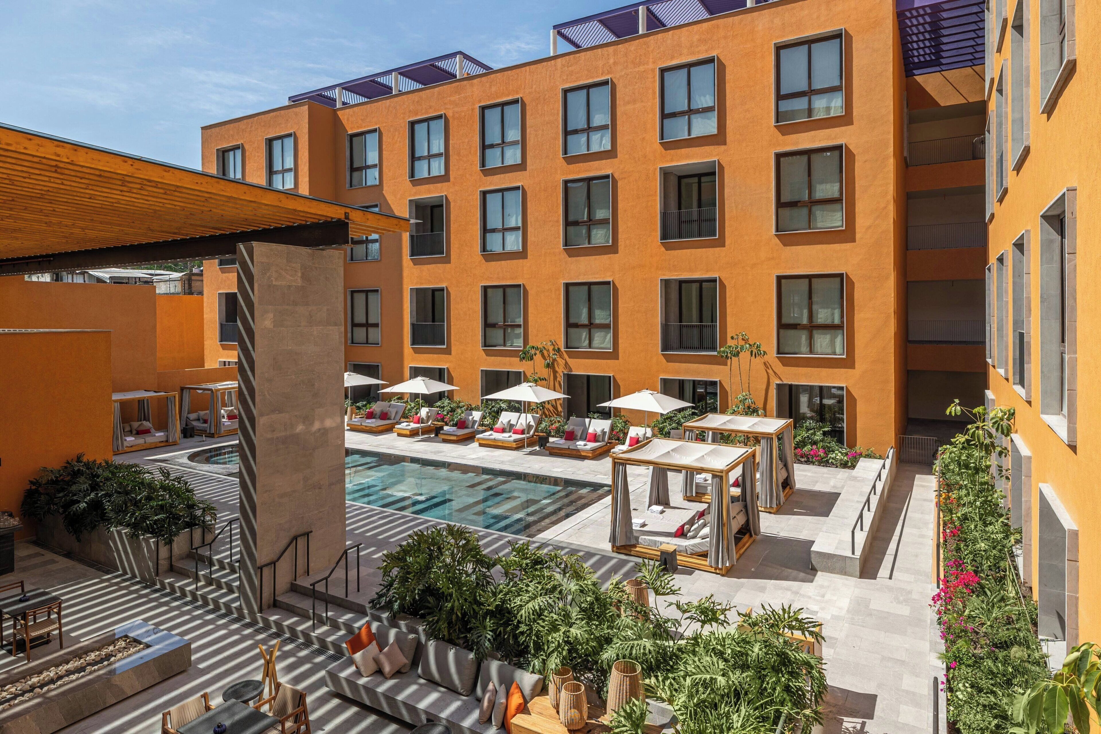 Ein modernes Hotel mit Poolbereich, Sitzgelegenheiten im Freien und einem Innenhof mit Pflanzen.