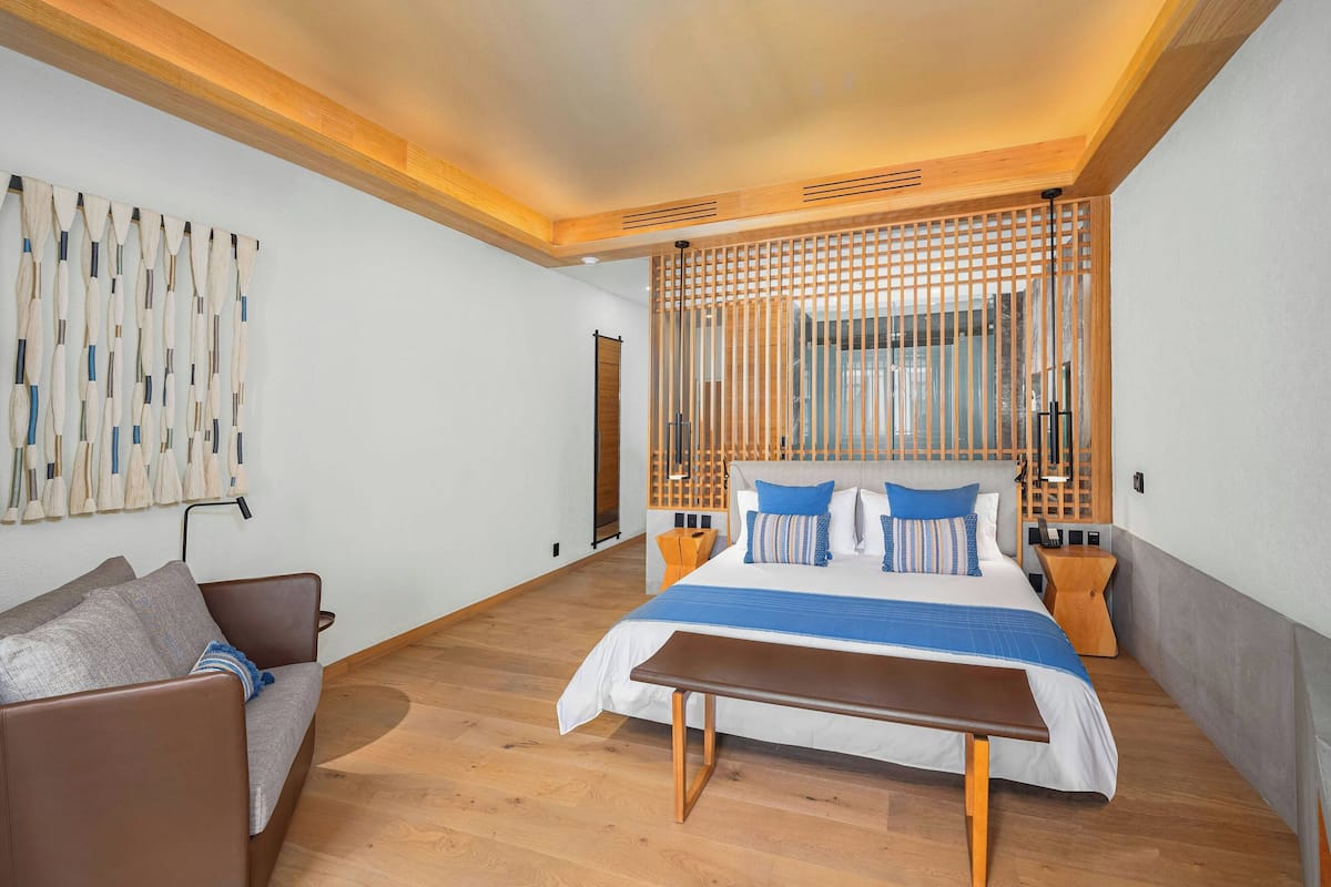 Un dormitorio moderno con una cama grande, cabecera de madera, una banca, un sofá y una obra de arte en la pared.