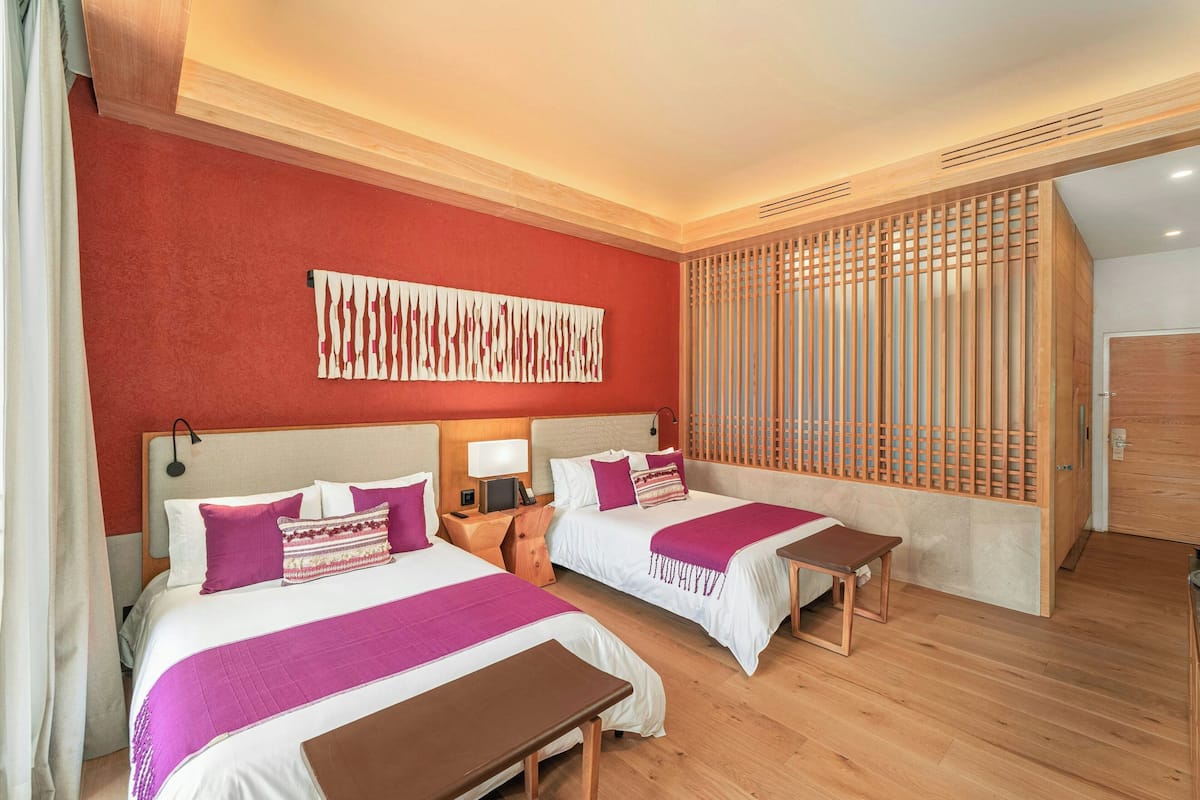 Una habitación de hotel con dos camas, pisos de madera, una pared de acento roja y una obra de arte abstracta de gran tamaño.