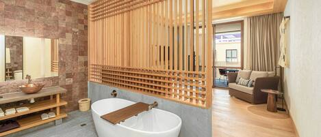 A modern bathroom with a freestanding bathtub, a wooden slatted partition, and a stone wall.
