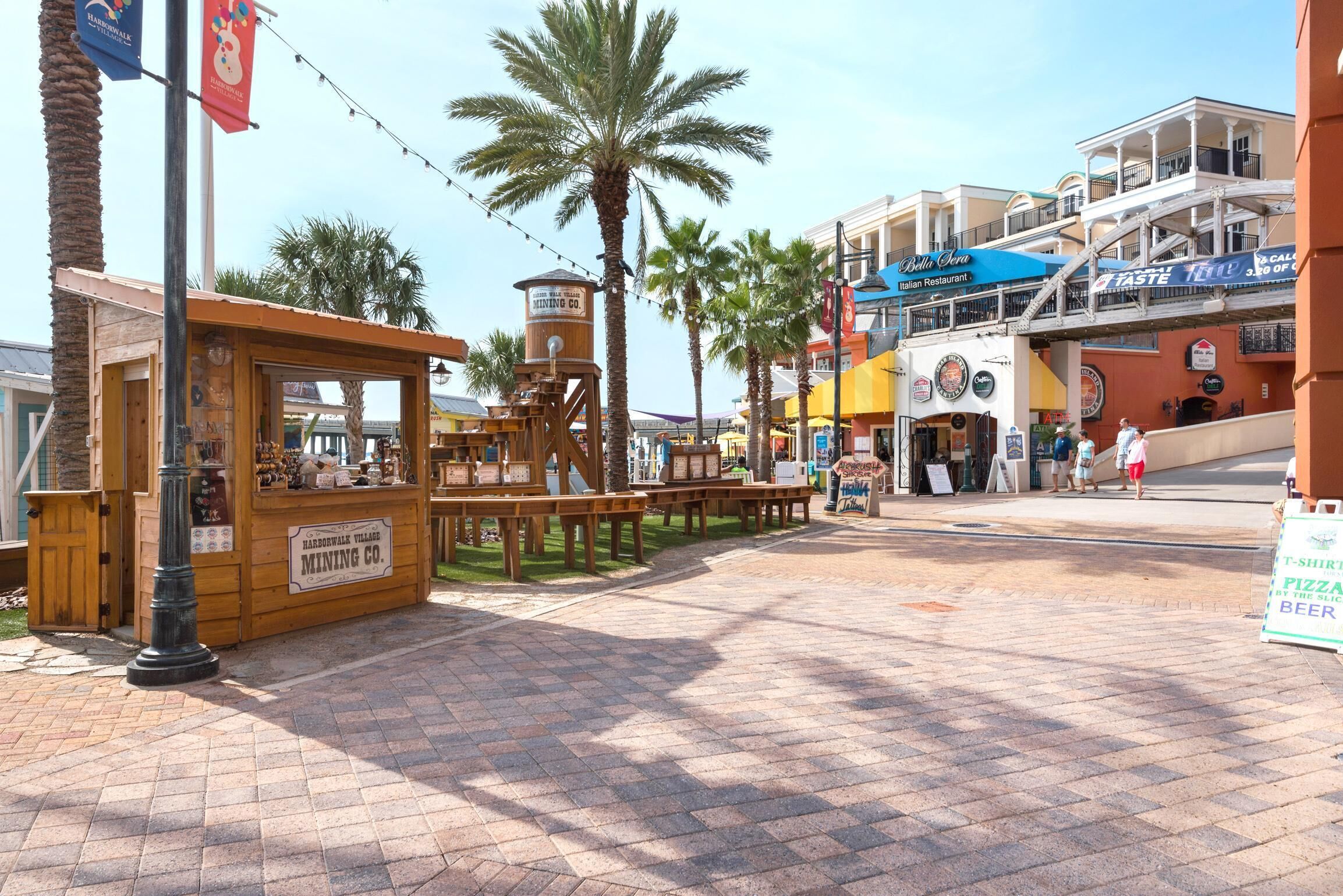 A street with a wooden mining exhibit, palm trees, and various shops including an Italian restaurant.