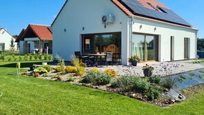 A modern house with a red-tiled roof, large windows, and a well-maintained garden with various plants and flowers. - Vacation home near Swinemünde, in the countryside / Baltic Sea, quiet location - dogs welcome (Kołczewo)