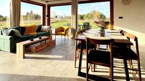 A spacious living area with a wooden dining table, chairs, a sofa, and a coffee table. There are large windows offering a view of the outdoors. - Vacation home near Swinemünde, in the countryside / Baltic Sea, quiet location - dogs welcome (Kołczewo)