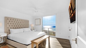 A bedroom with a large bed, a wooden bench, a nightstand, and a view of the ocean. - Shoreline Towers 1066 (Destin)
